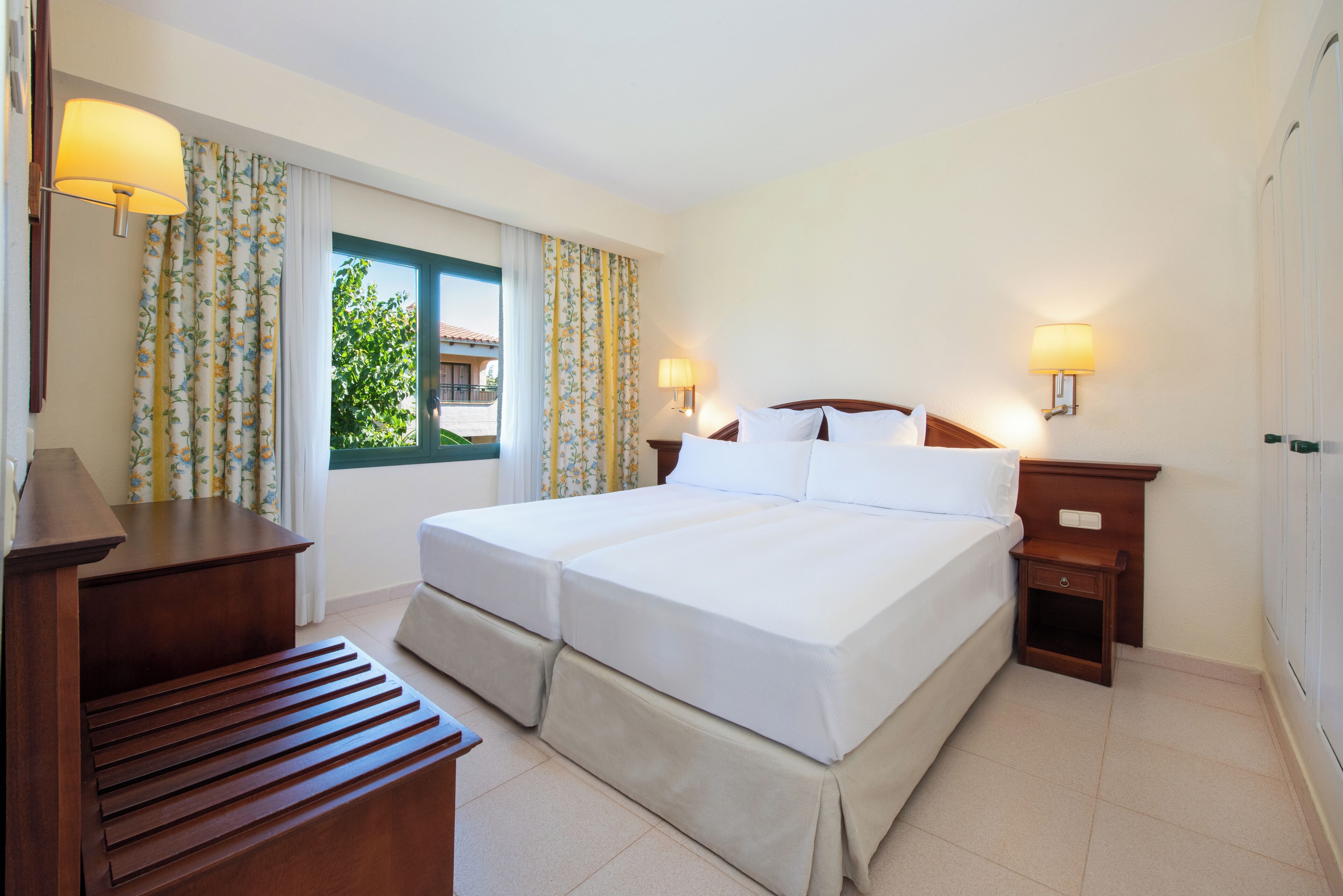 A hotel room with two beds, a wooden desk, and a window with curtains.
