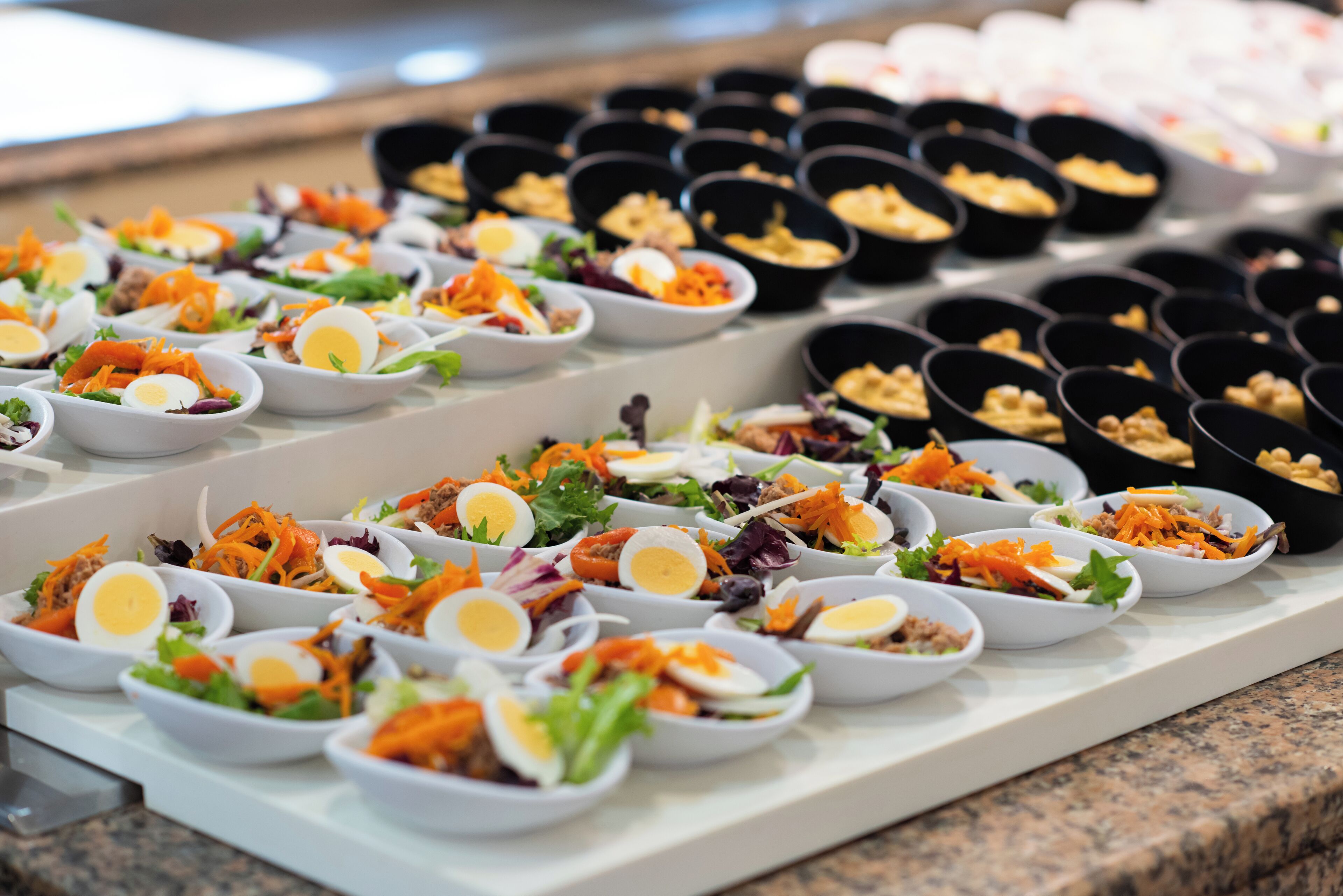 Un bufé con diversos platos, incluyendo ensaladas, huevos y otros alimentos ya preparados.