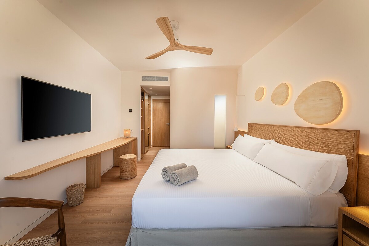 A modern hotel room with a large bed, a flat-screen TV, a wooden headboard, and a ceiling fan.