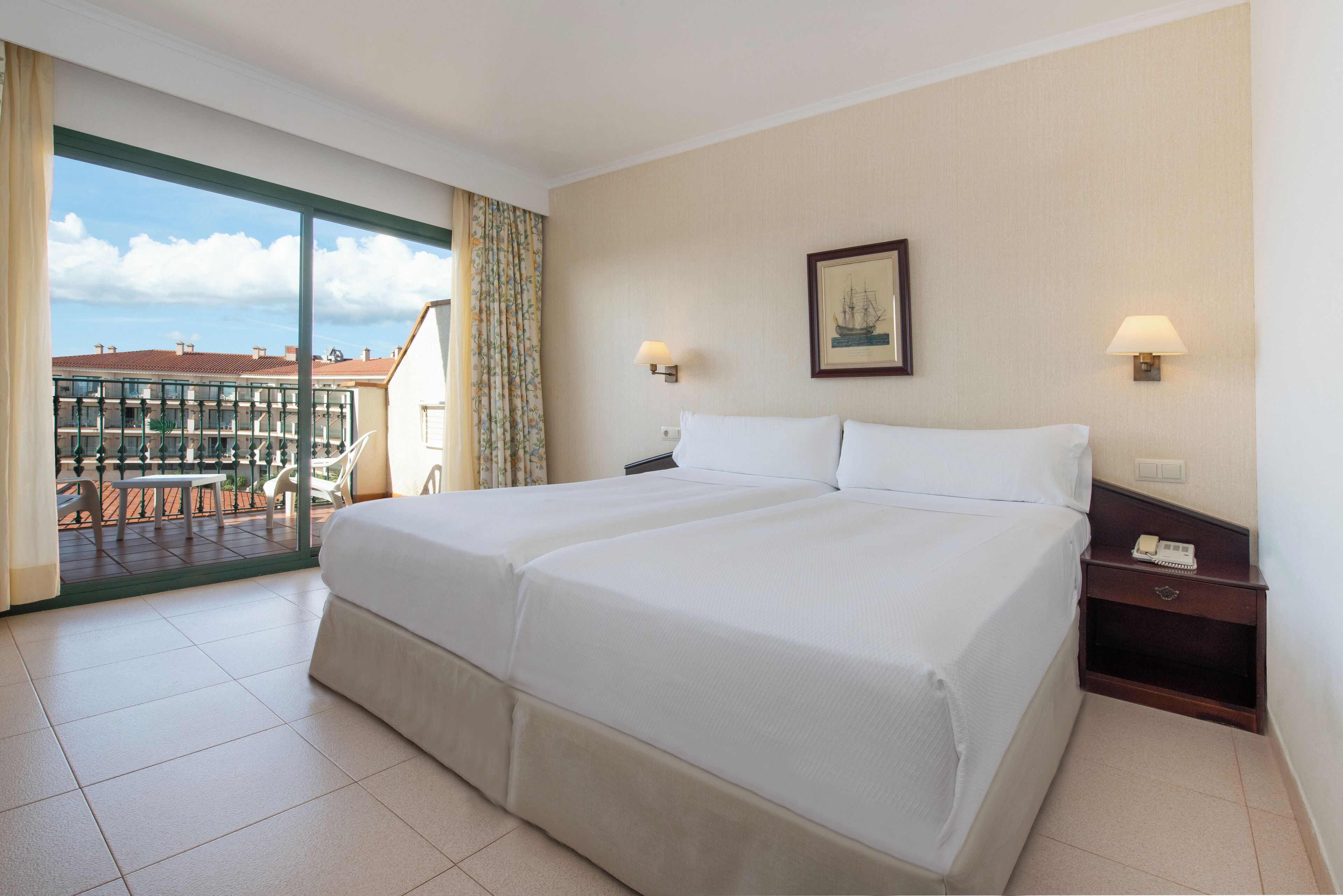 Una habitación de hotel con una cama grande, dos mesitas de noche y vistas al balcón exterior.