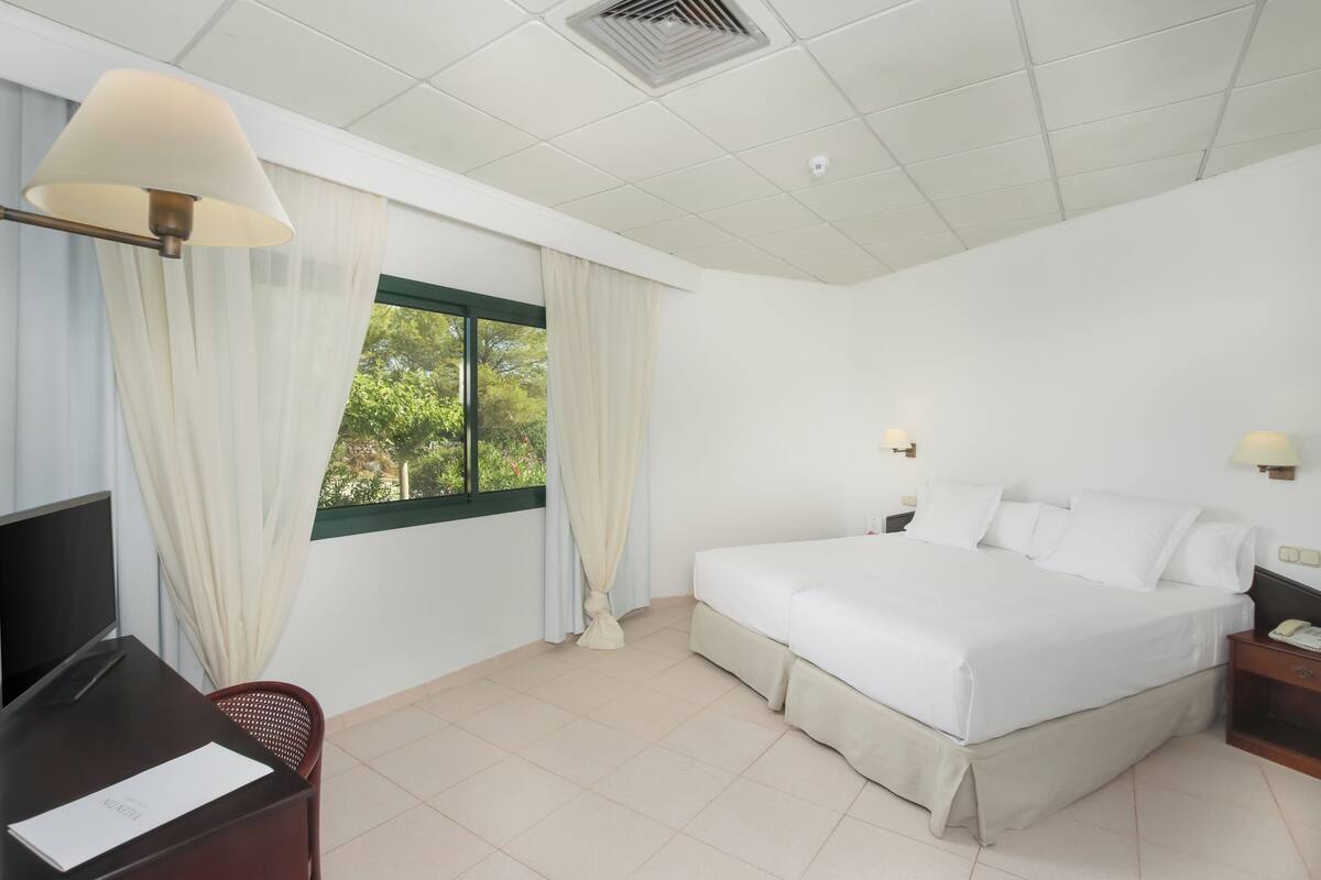 A hotel room with a bed, a desk, a chair, a TV, and a window with curtains.