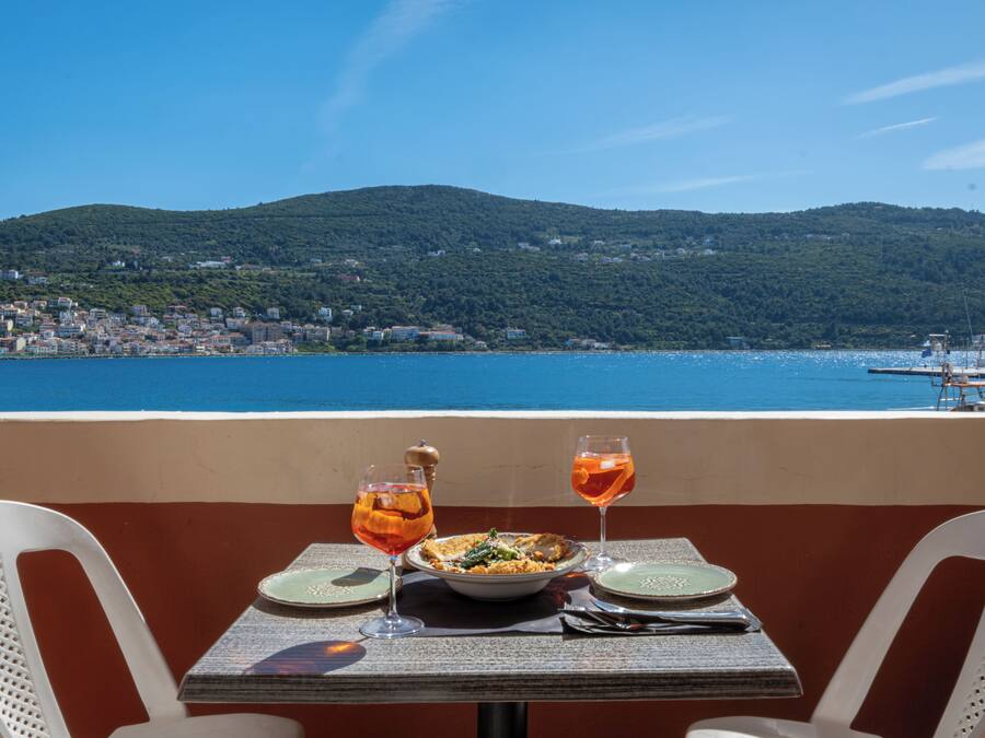 A table with a meal and drinks, overlooking a coastal town and hills.