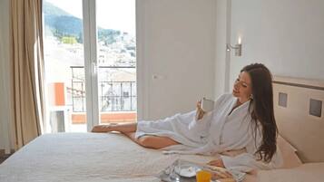 Habitación de hotel con una cama, una bandeja con productos para el desayuno y vistas a edificios y montañas a través de la ventana.