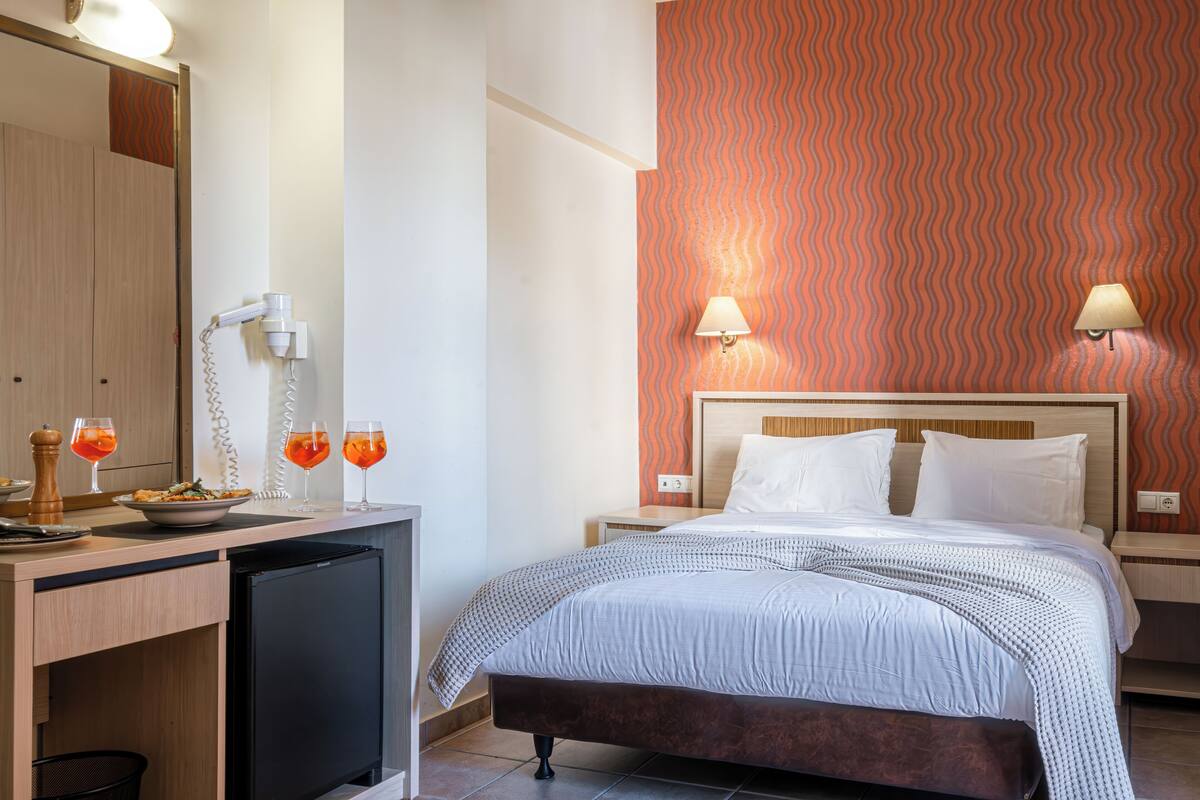 A hotel room with a bed, bedside tables, a desk with a mini-fridge, and a mirror.