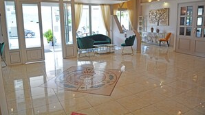 A spacious lobby with a tiled floor, a green sofa, a marble coffee table, and a painting on the wall. - Samos Hotel  (Samos)