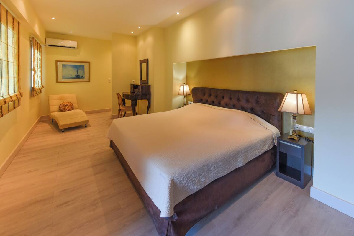A hotel room with a large bed, a desk, a chair, and a lamp.