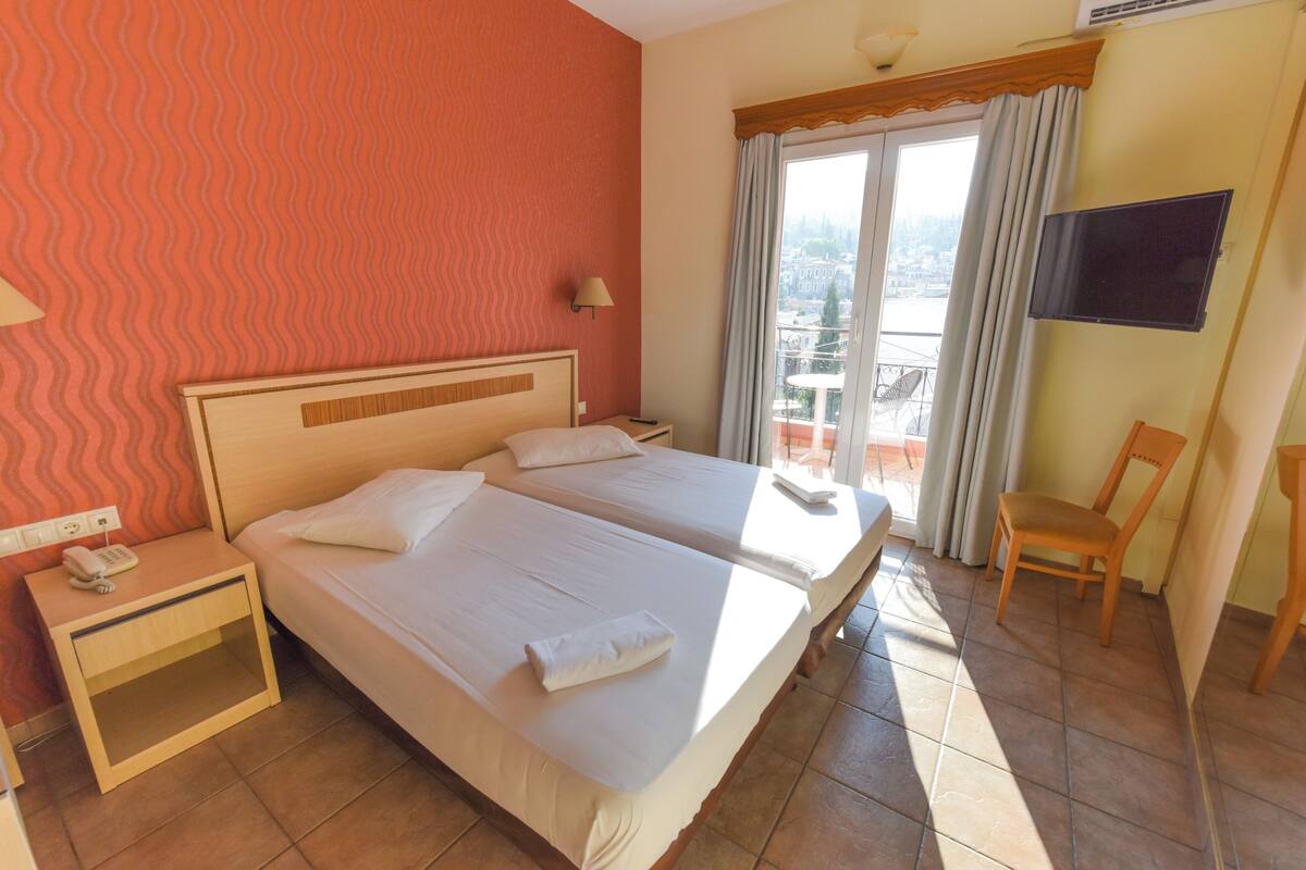A hotel room with two beds, a nightstand with a phone, a chair, a TV, and a balcony with a view.