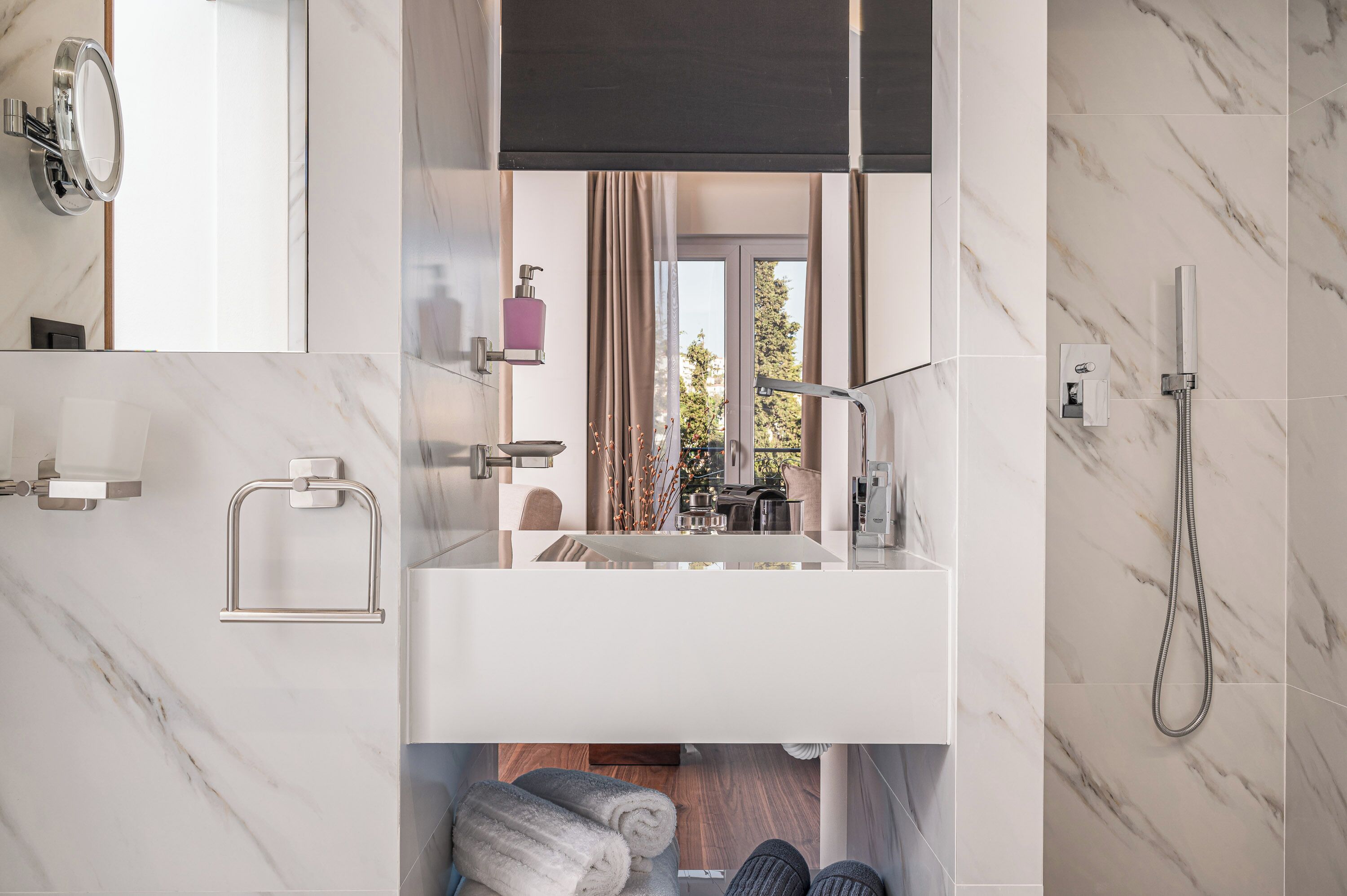 Ein modernes Badezimmer mit großem Spiegel, integriertem Waschbecken, Dusche und Blick ins Freie.