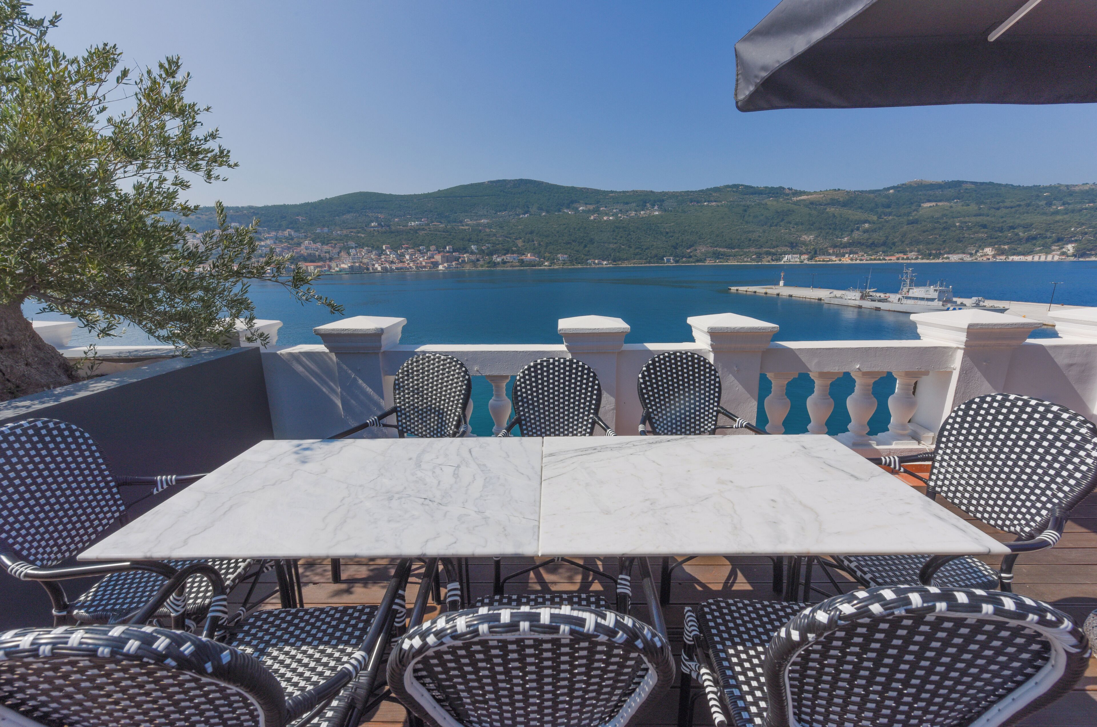 Terraço com mesa e cadeiras com vista para um corpo d'água e uma cidade distante.