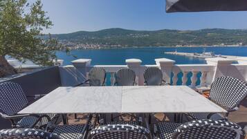 Terraço com mesa e cadeiras com vista para um corpo d'água e uma cidade distante.