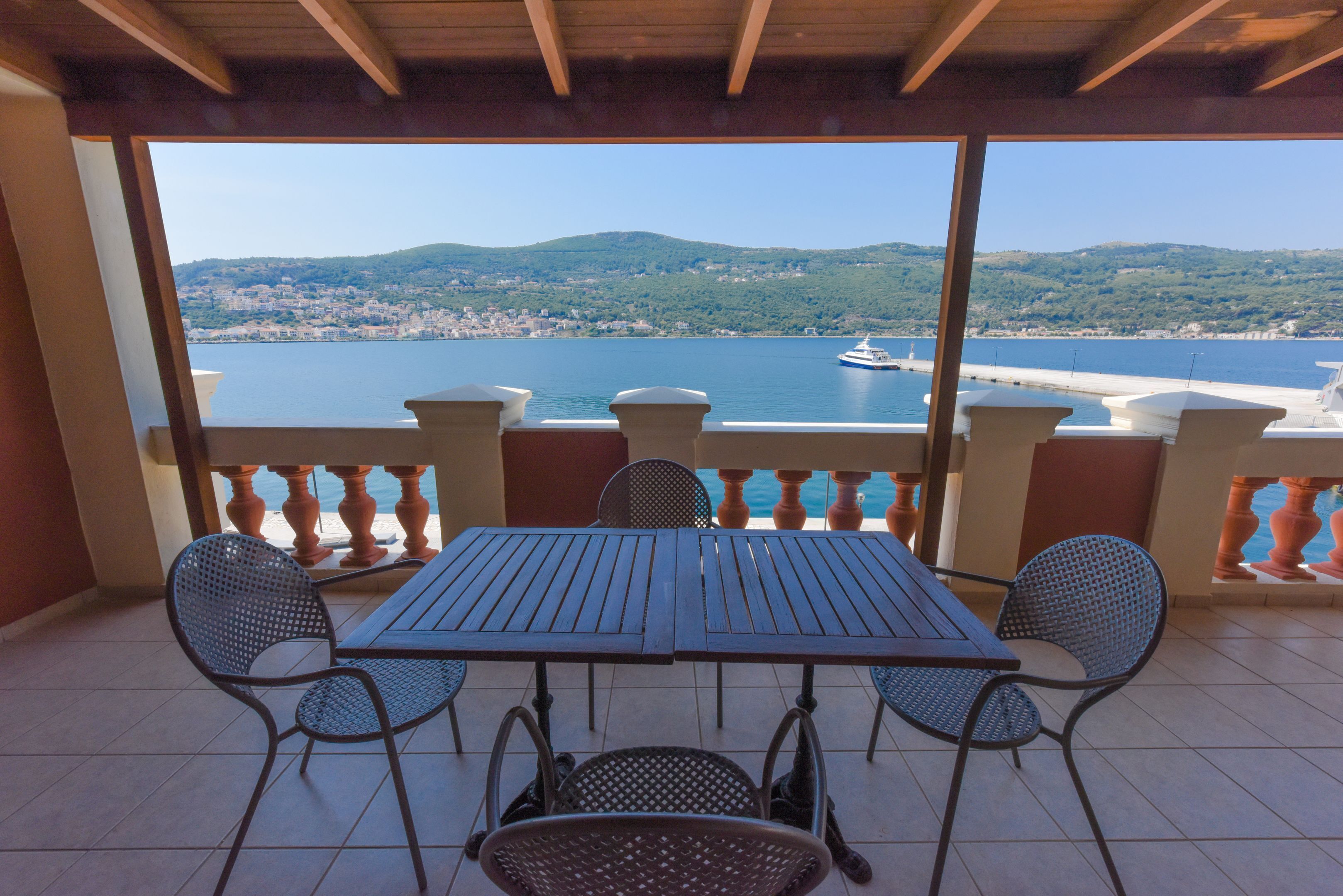 A balcony with a table and chairs overlooking a body of water and a distant town.