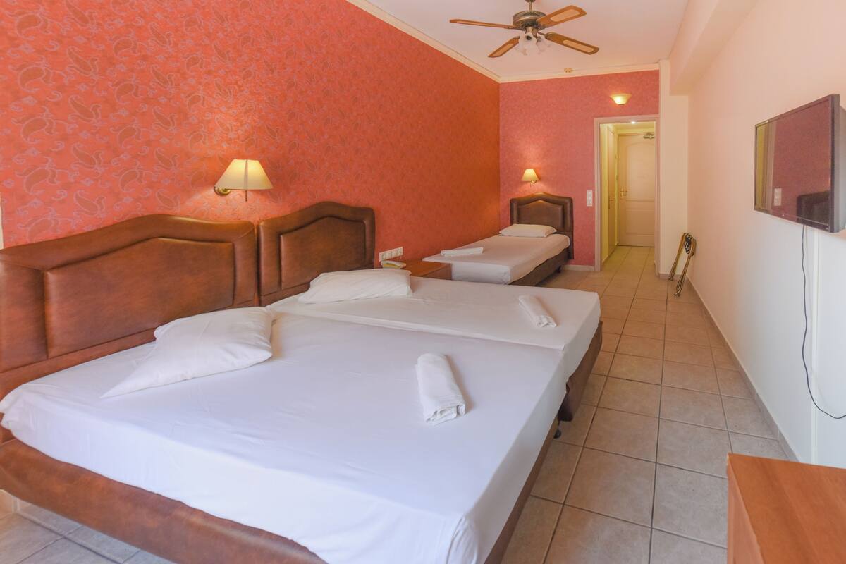 A hotel room with two beds, a ceiling fan, and a TV on the wall.