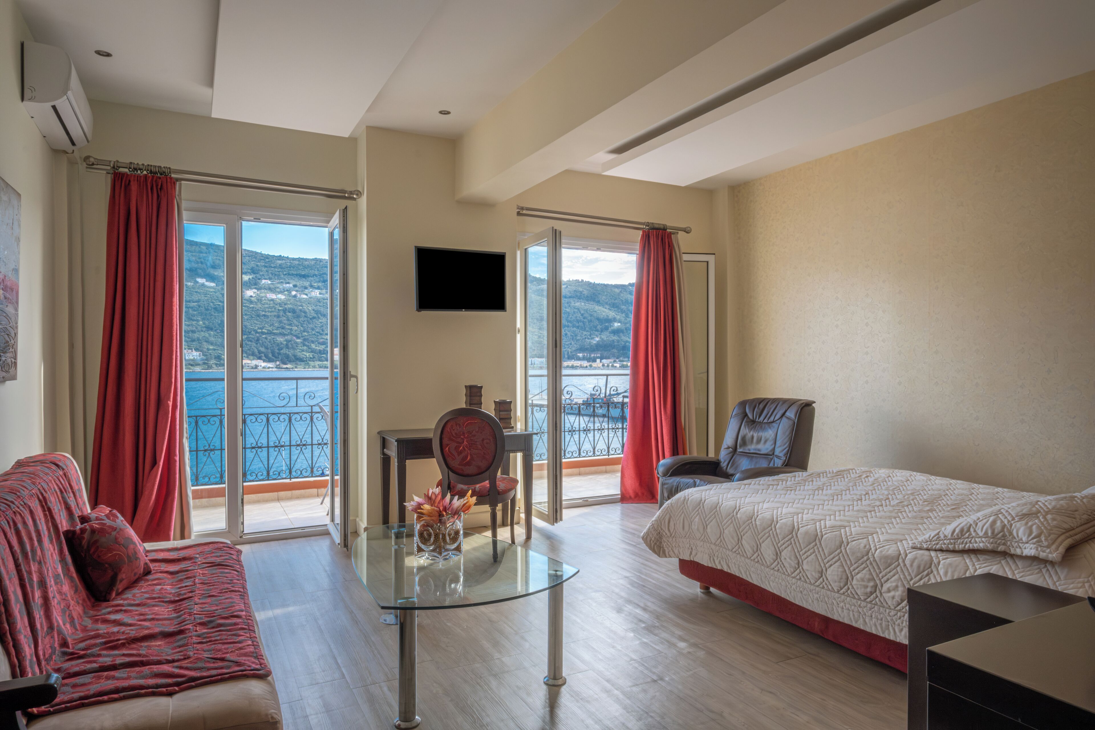 Une chambre d’hôtel avec un balcon, un lit, un canapé, une télévision et une table agrémentée d’un vase.