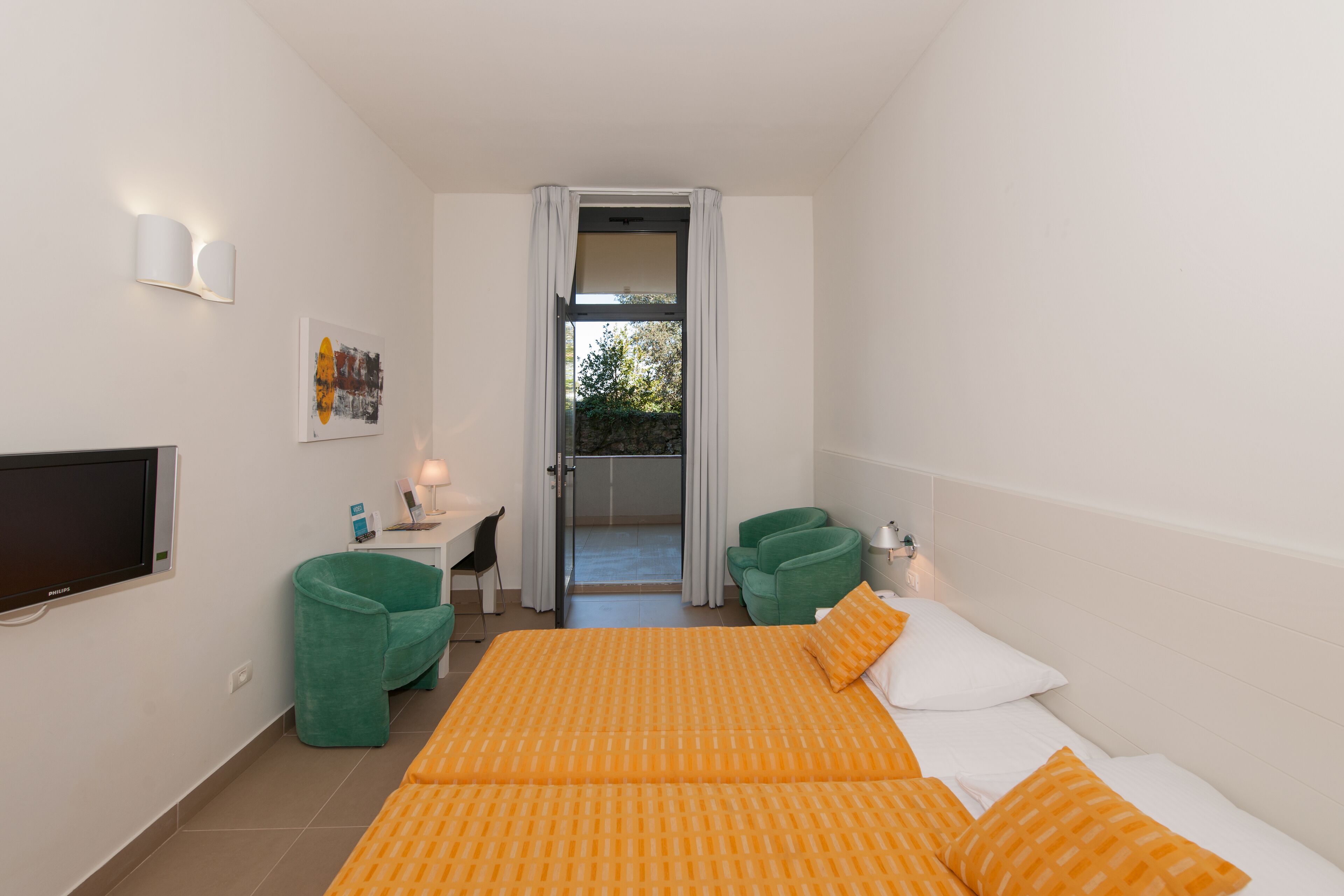 Habitación de hotel con cama, escritorio, silla, televisión y vistas al exterior.
