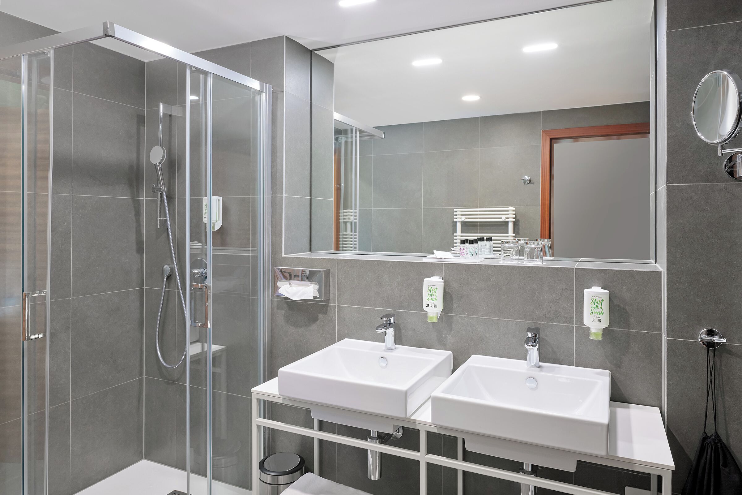 A modern bathroom with a glass-enclosed shower, two sinks, a mirror, and a towel rack.