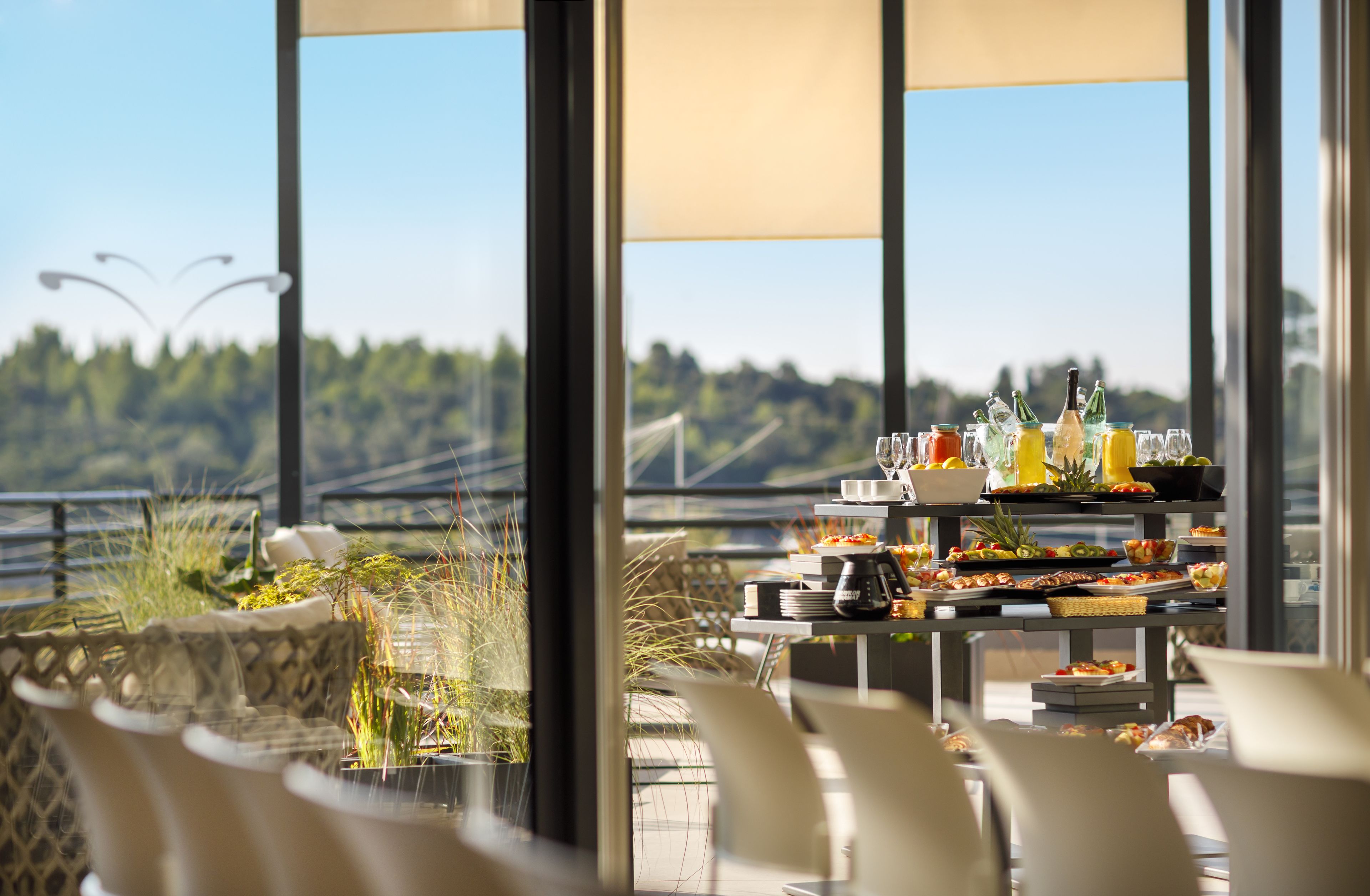 A dining area with a view of a bridge and greenery, featuring a buffet with various dishes and drinks.