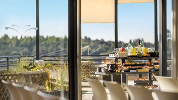 A dining area with a view of a bridge and greenery, featuring a buffet with various dishes and drinks.