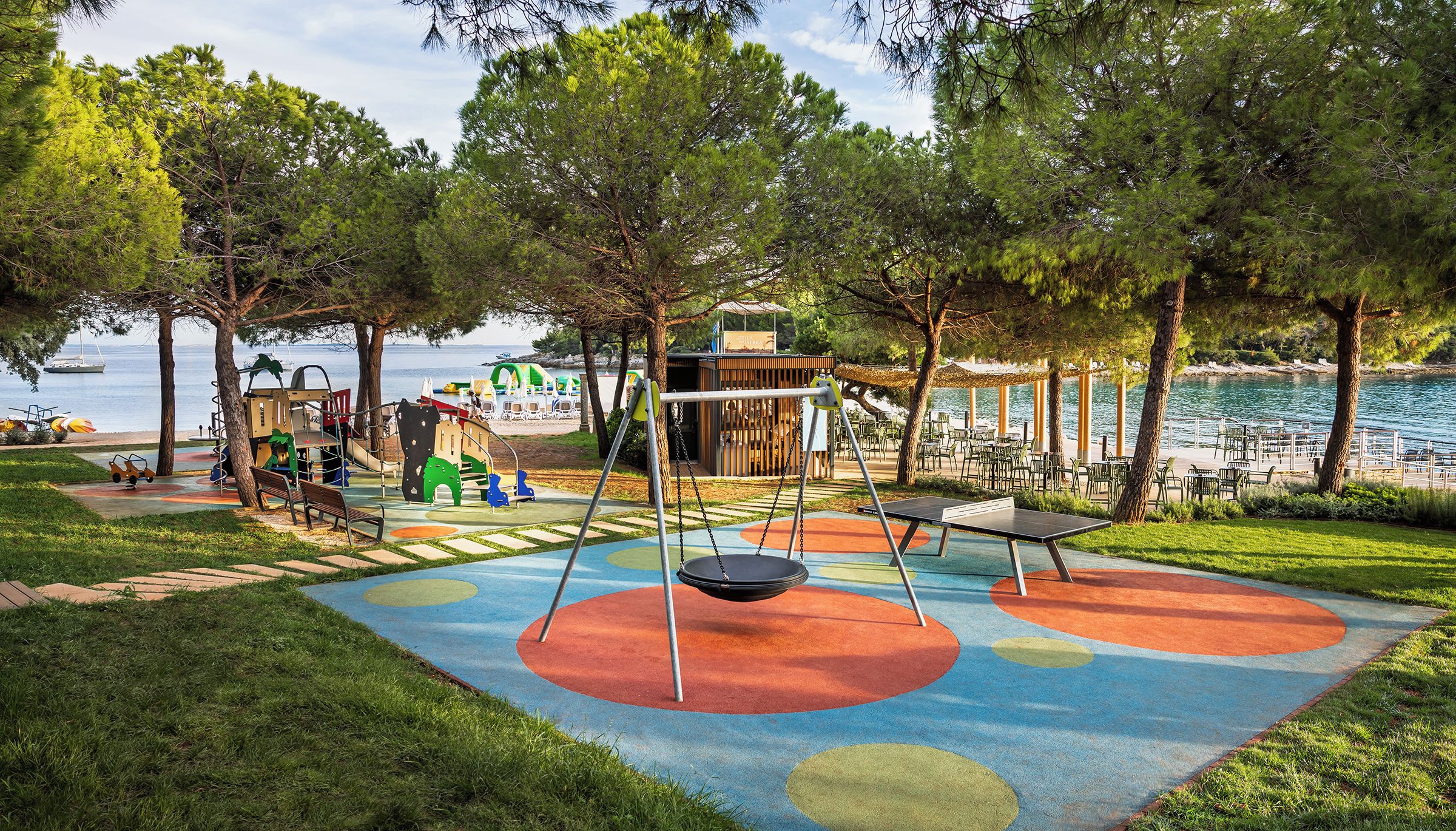 A playground with swings and slides, a picnic area, and a view of the sea.