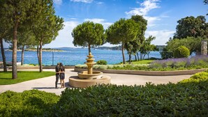 A landscaped area with a fountain, trees, and a view of the sea. - Maistra Select Island Hotel Istra (Rovinj)