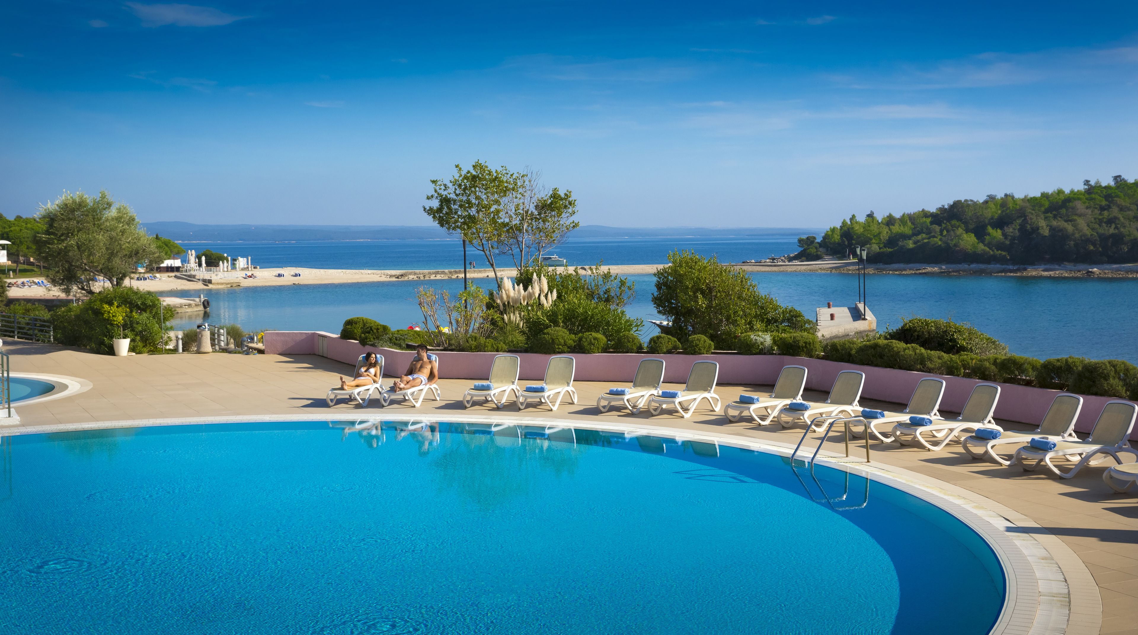 A pool with lounge chairs and a view of the sea.