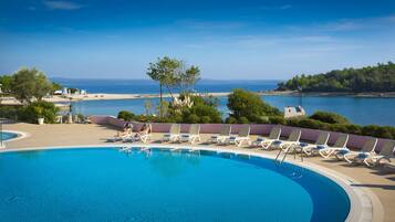 A pool with lounge chairs and a view of the sea.