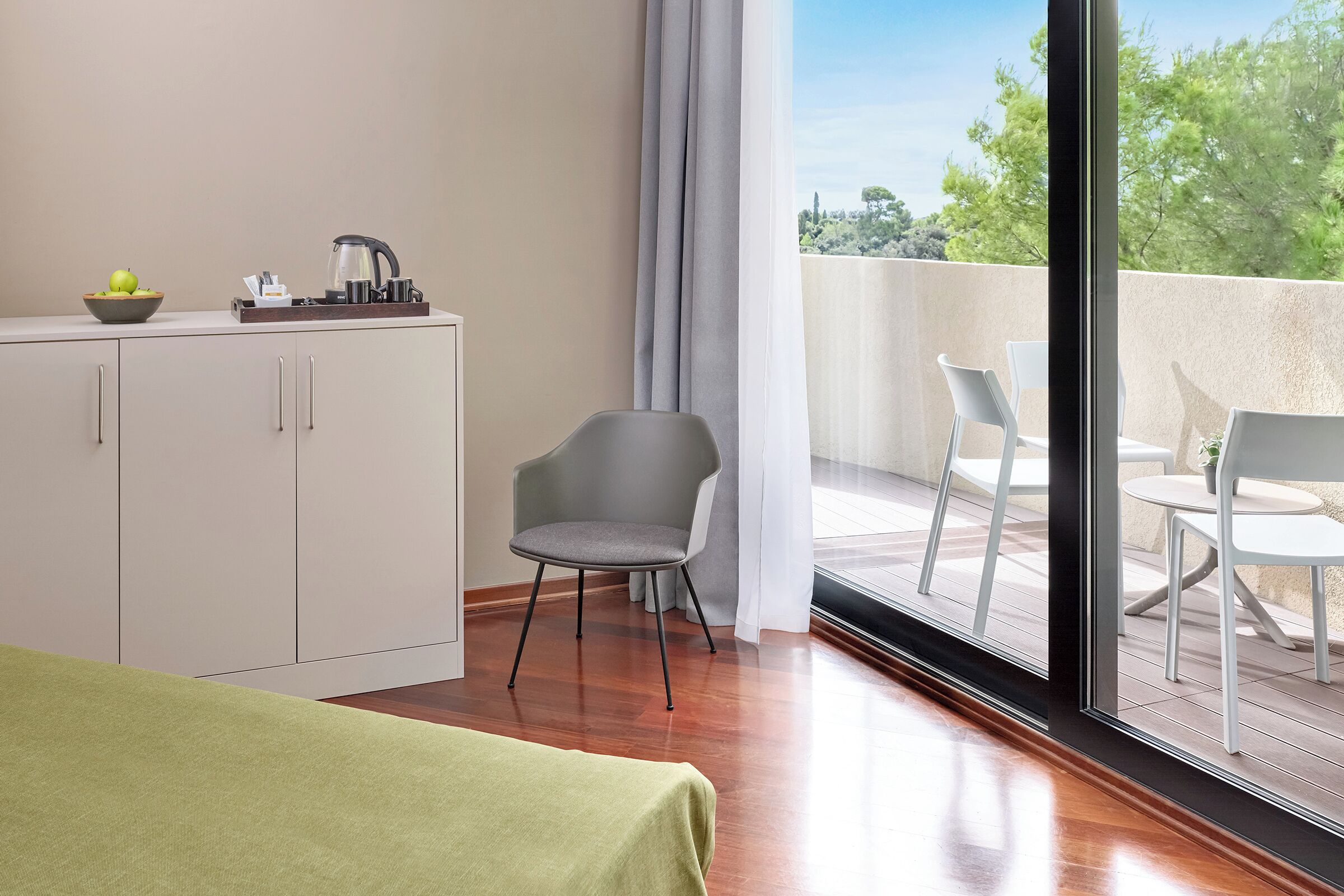 A modern hotel room with a balcony, a dining area, and a kitchenette.