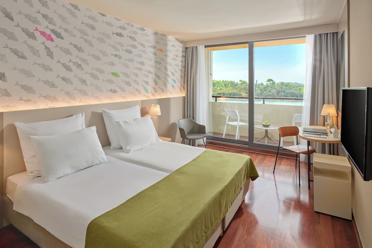 A hotel room with two beds, a balcony with a view, a desk with a chair, and a television.
