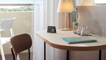 Habitación de hotel con balcón, una mesa con lámpara, una botella de agua y un cartel con un código QR.