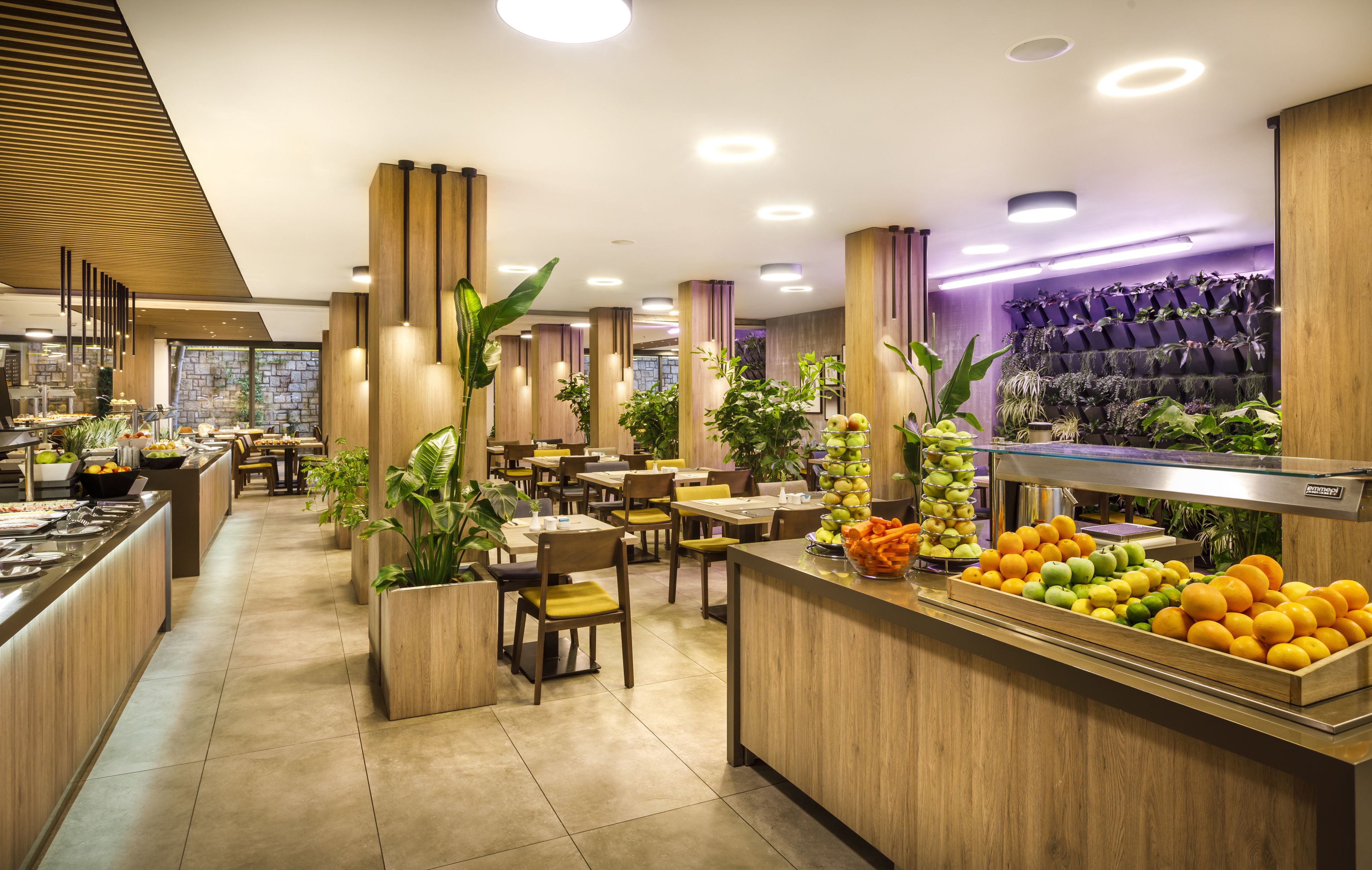 A modern restaurant with wooden decor, a variety of seating options, and a fruit display.
