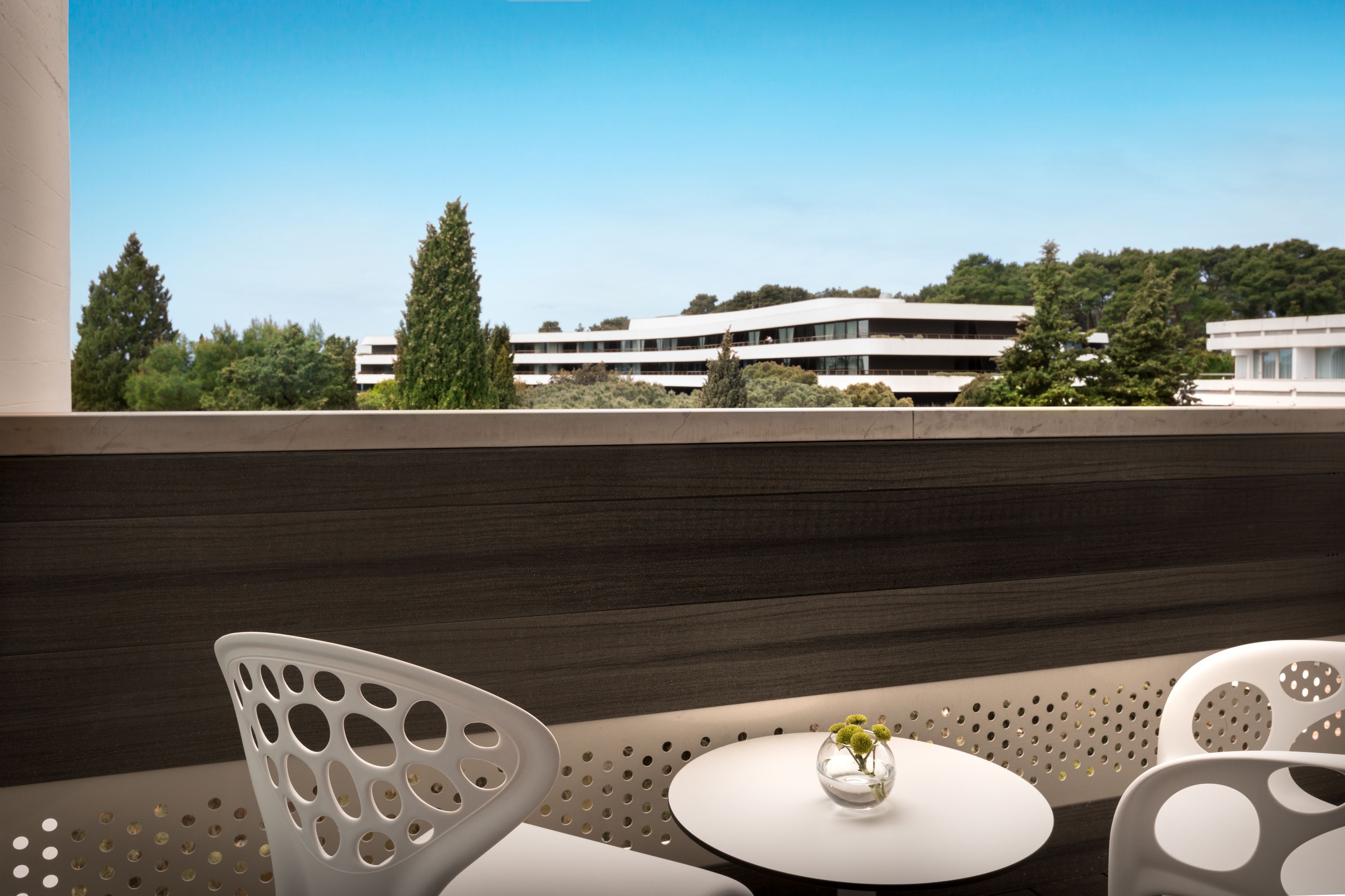 A modern interior with a balcony overlooking a building and trees.