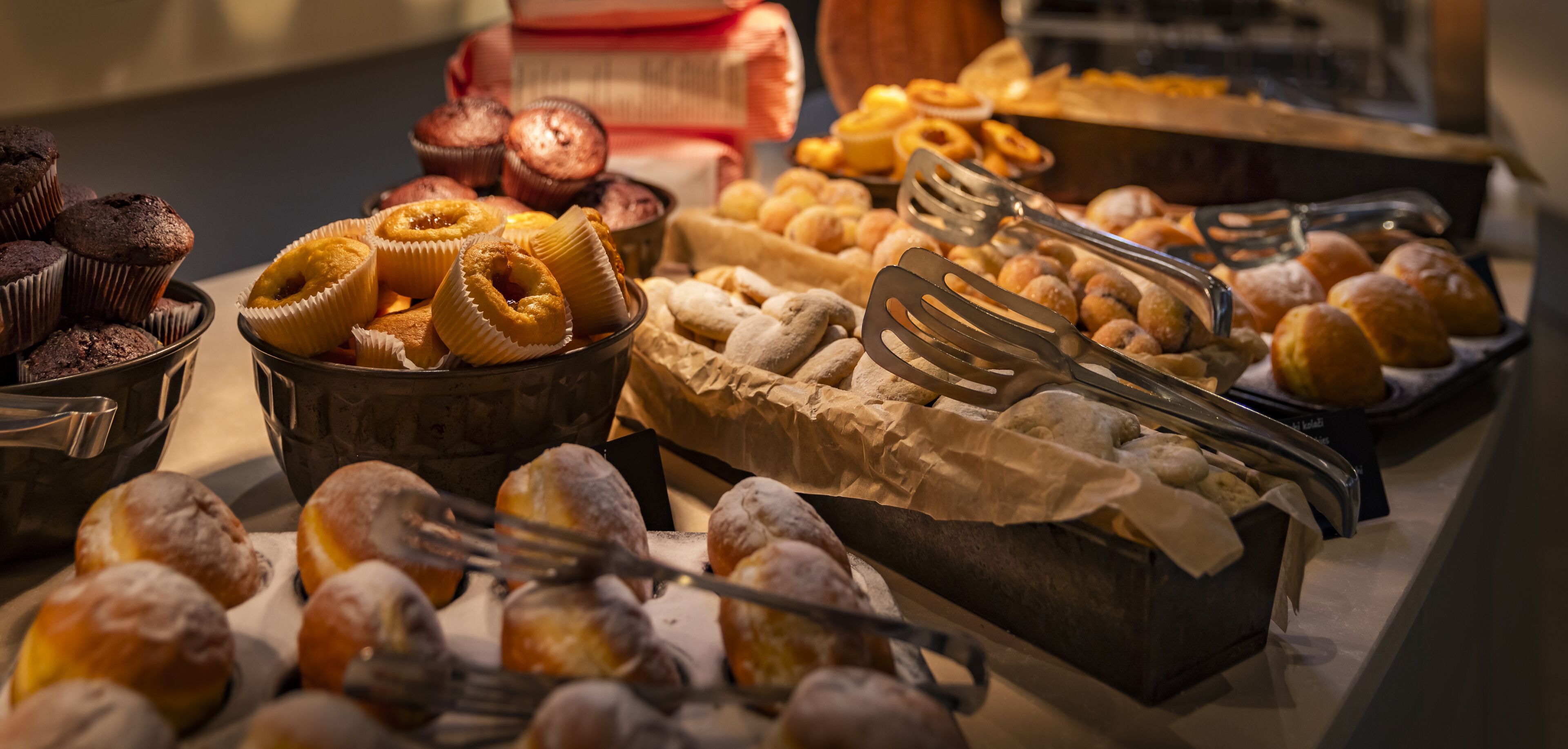 Eine Auswahl an Backwaren auf einer Theke, darunter Muffins, Donuts und Gebäck.