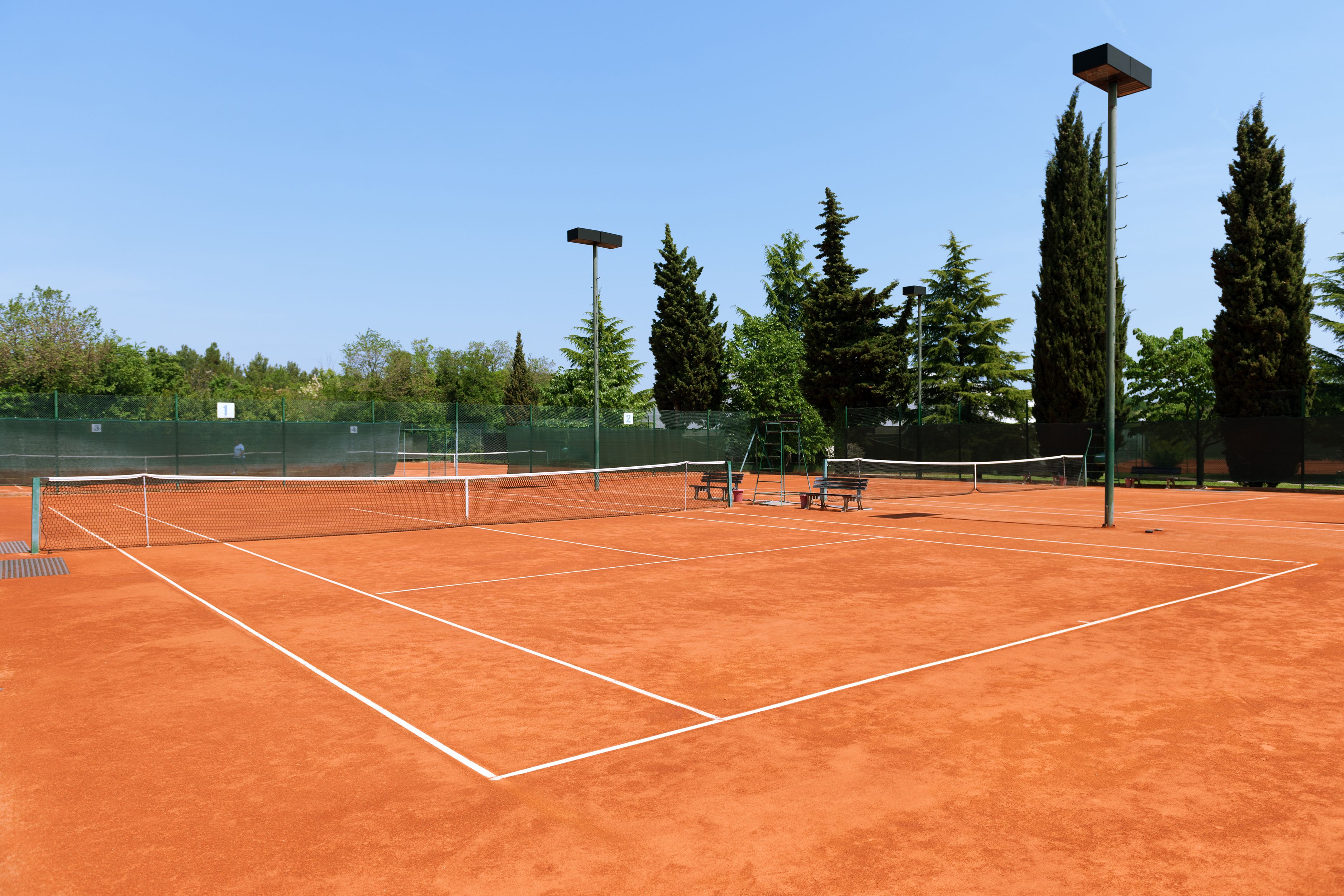 A tennis court with a net, benches, and floodlights.