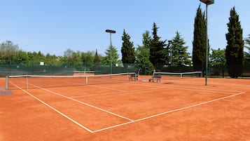 A tennis court with a net, benches, and floodlights.