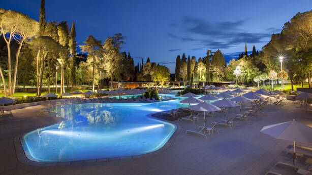 A swimming pool with lounge chairs and umbrellas, surrounded by trees and a night sky. - Eden Hotel by Maistra Collection (Rovinj)