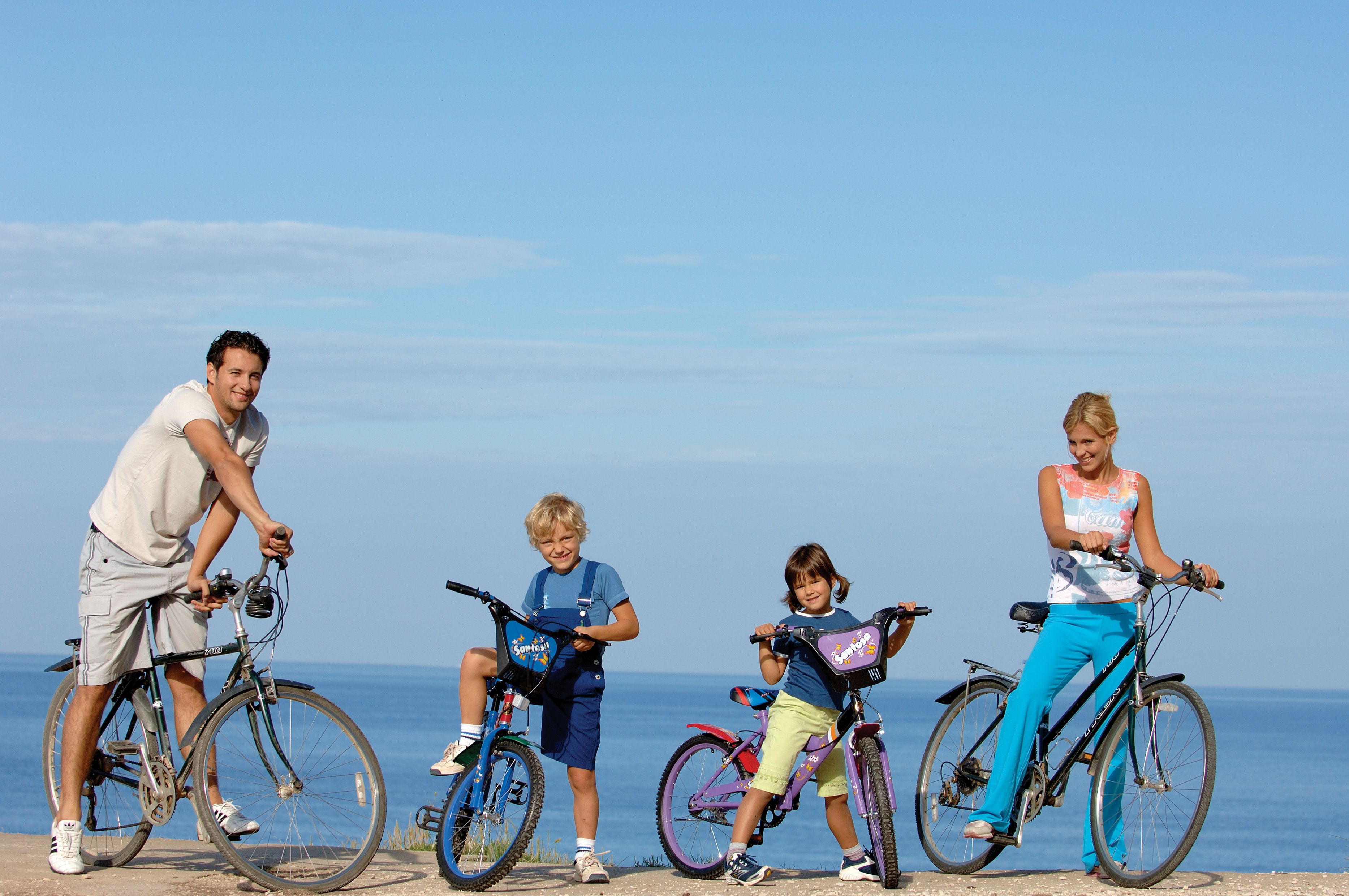 Cuatro personas en bicicletas junto al mar, bajo un cielo despejado.