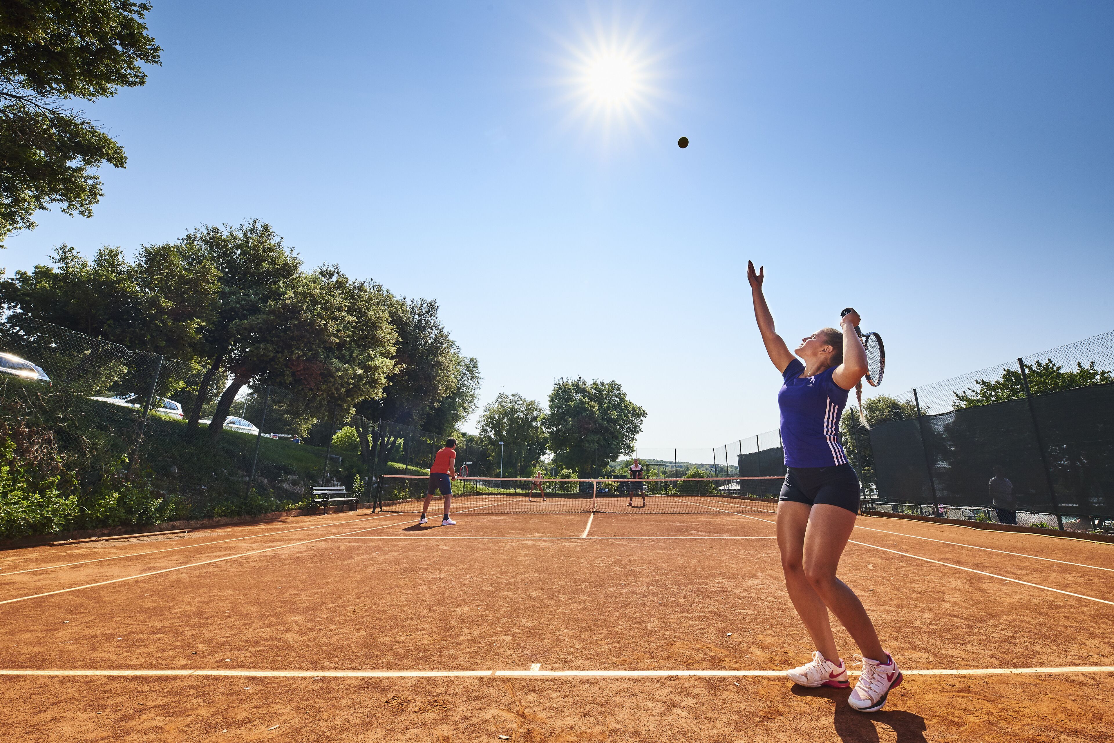 A tennis court with a net in the center, surrounded by trees and a fence.