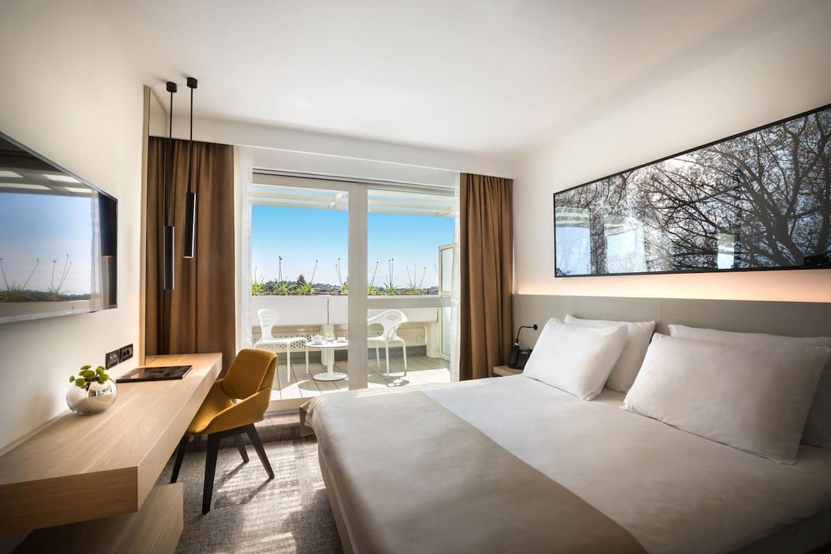 A hotel room with a bed, a desk, a chair, a table, and a large window with a view.