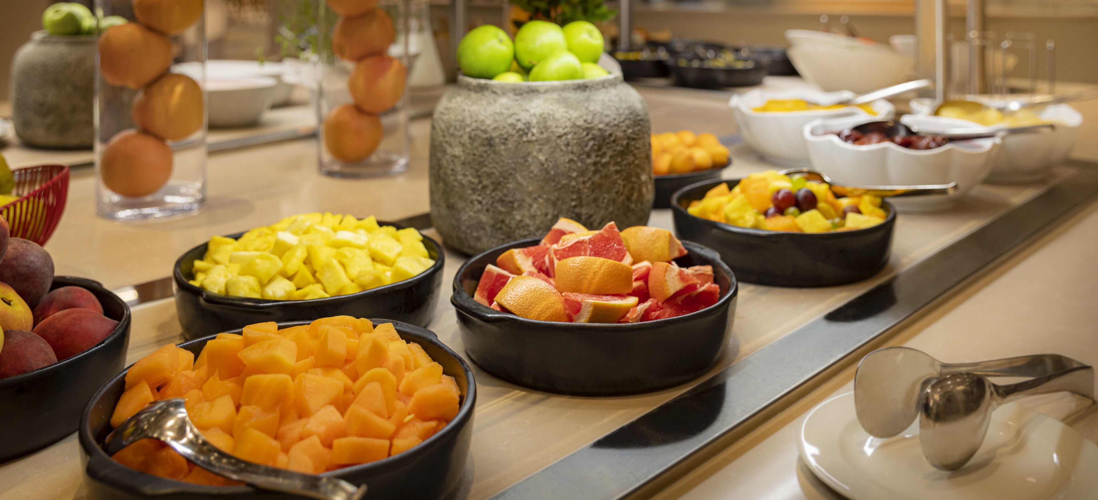 A buffet with various fruits and vegetables in black bowls.