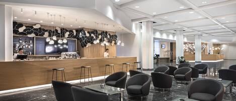 Um lobby moderno de hotel com balcão de recepção, área de bar e disposição de assentos.