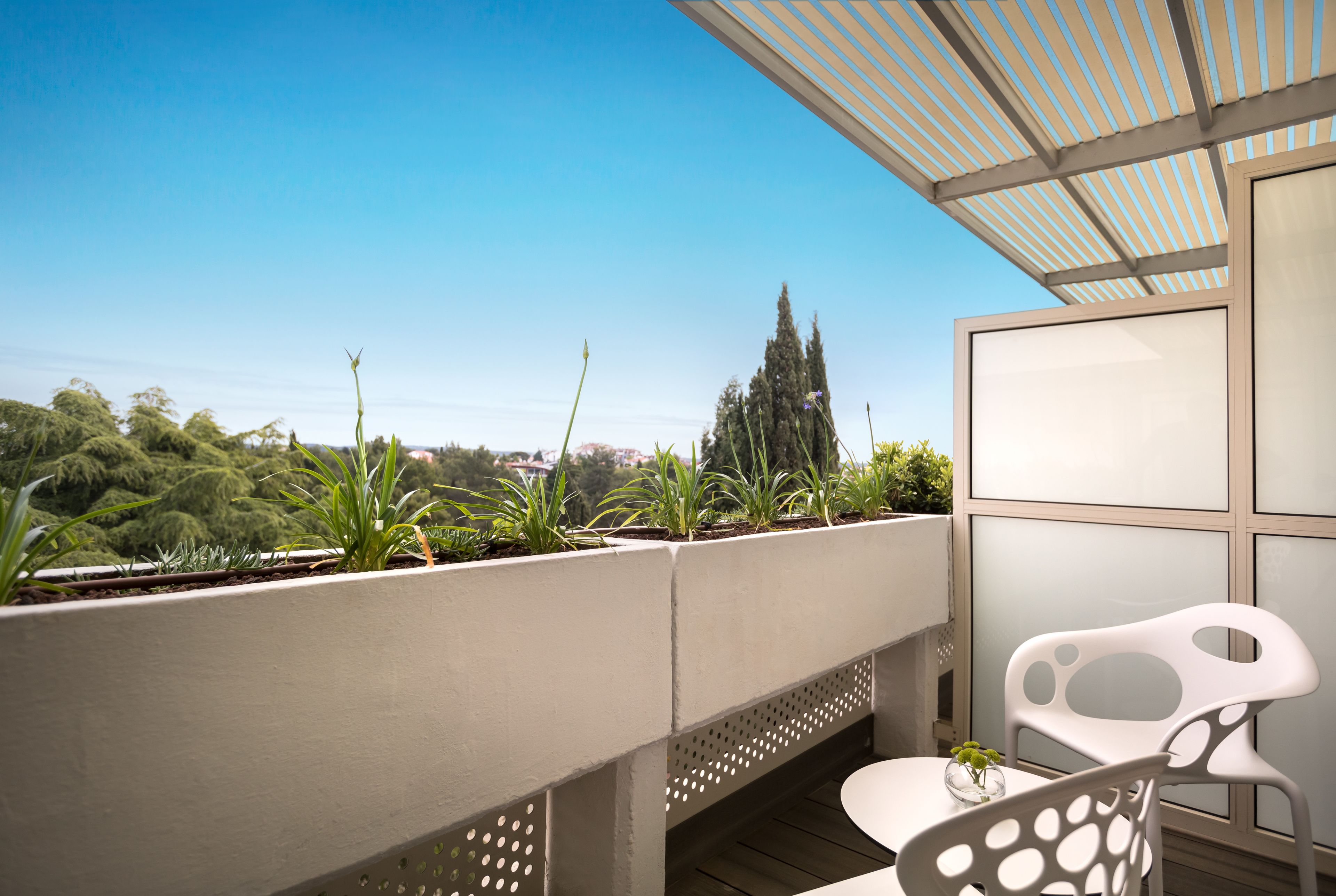 A balcony with a white chair, a small table, and a potted plant.