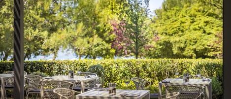 An outdoor dining area with tables and chairs, surrounded by greenery and trees.