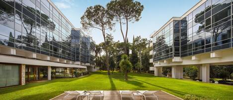Un edificio moderno con amplios ventanales, césped cuidado y zona de estar al aire libre.