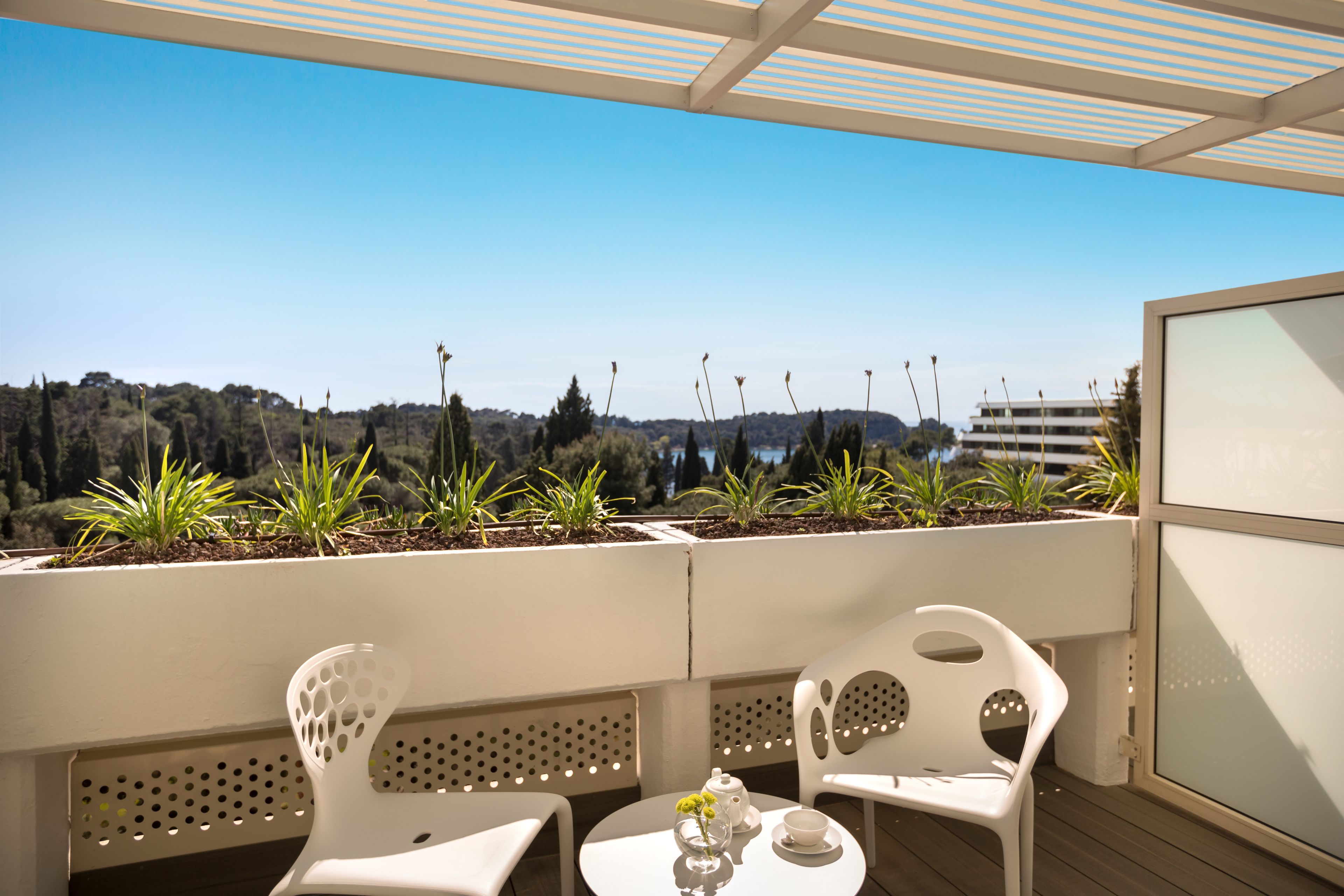 A terrace with white chairs, a table, and a view of a forested landscape.