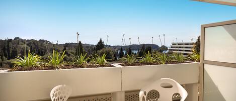 A terrace with white chairs, a table, and a view of a forested landscape.