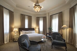 Una habitación de hotel con una cama grande, dos sillones, una mesita, una lámpara de pie y una araña.