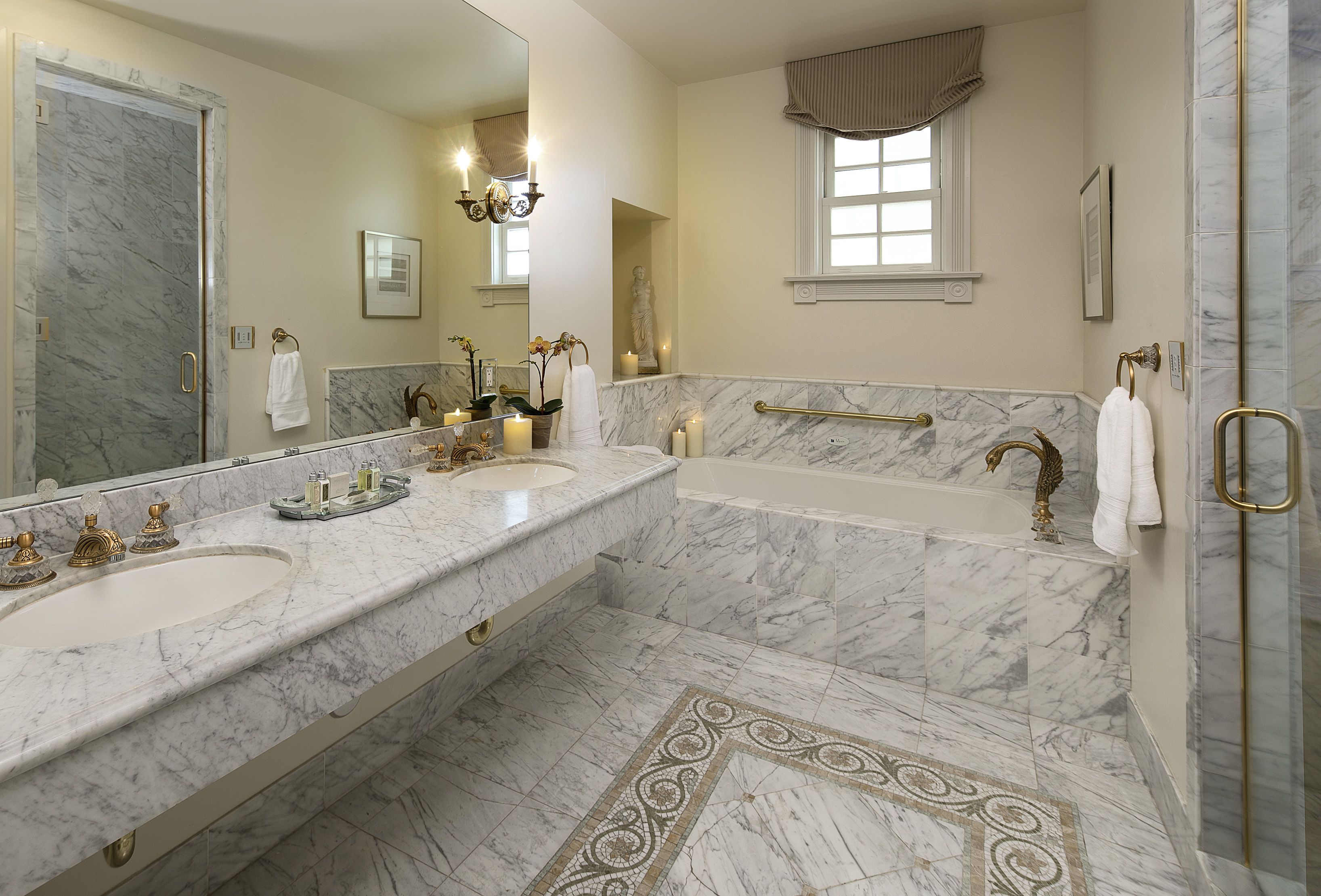 A luxurious bathroom with marble countertops, a large mirror, a bathtub, and a shower area.
