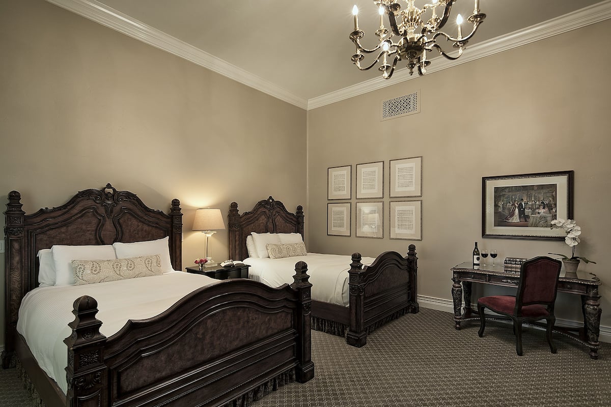 A traditional bedroom with two beds, a desk, and a chair.