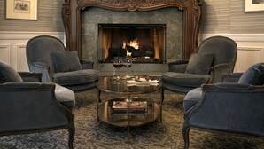 A cozy living room with a fireplace, two armchairs, a coffee table, and a bookshelf. - The Genevieve (Santa Ynez)