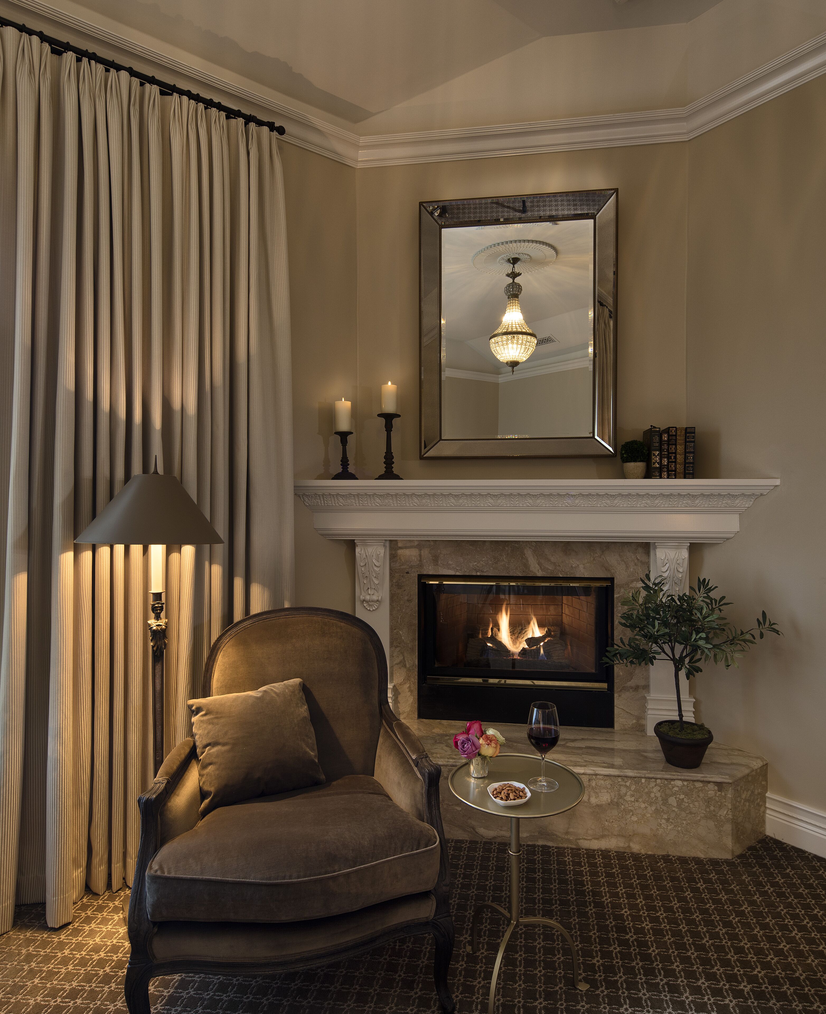 Een gezellige woonkamer met een open haard, een comfortabele fauteuil, een klein tafeltje met een glas wijn en een kamerplant.
