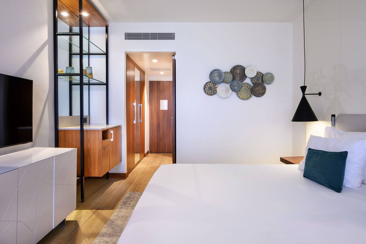 Ett modernt hotellrum med en stor säng, en TV, en garderob i trä och en vägg dekorerad med prydnadstallrikar.